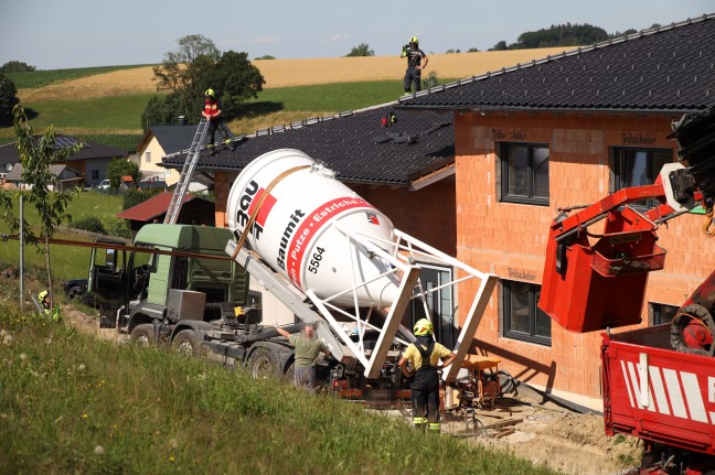 LKW-Bergung in Regau: LKW mit Putzsilo gegen Hausfassade gekippt